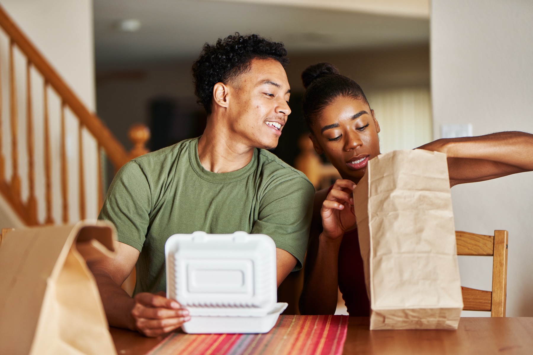 Two people opening a takeaway meal together at a table